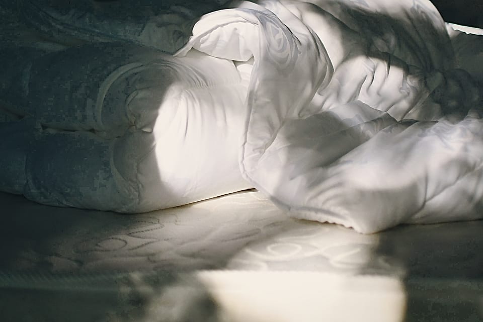 Couette repliée sur un matelas, dans la lumière du matin